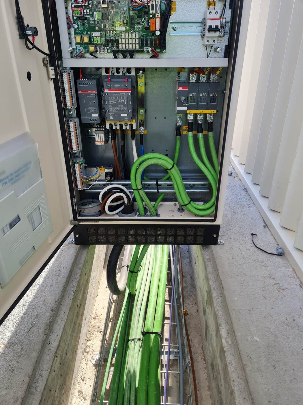 Cuadro eléctrico de exterior abierto sobre una zanja con cables de potencia